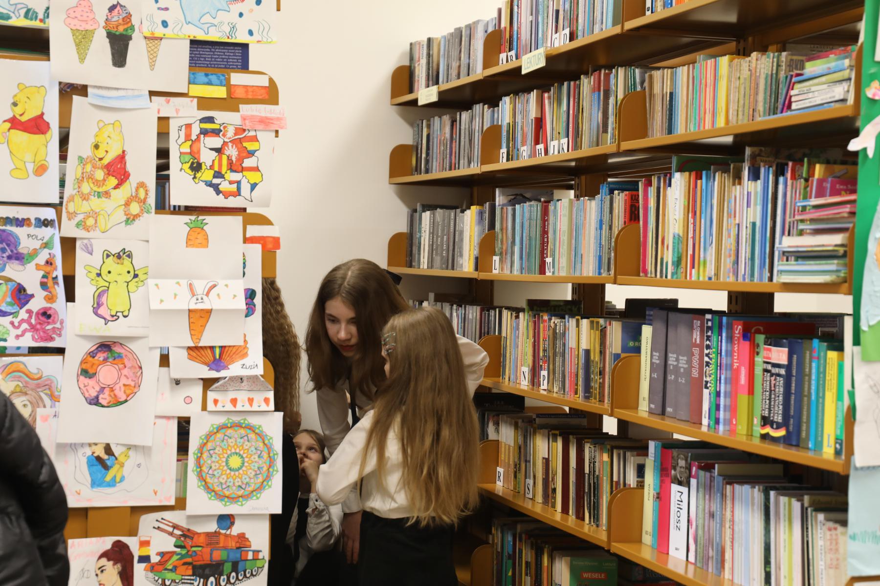 Na zdjęciu znajdują się uczennice, oglądające książki w bibliotece