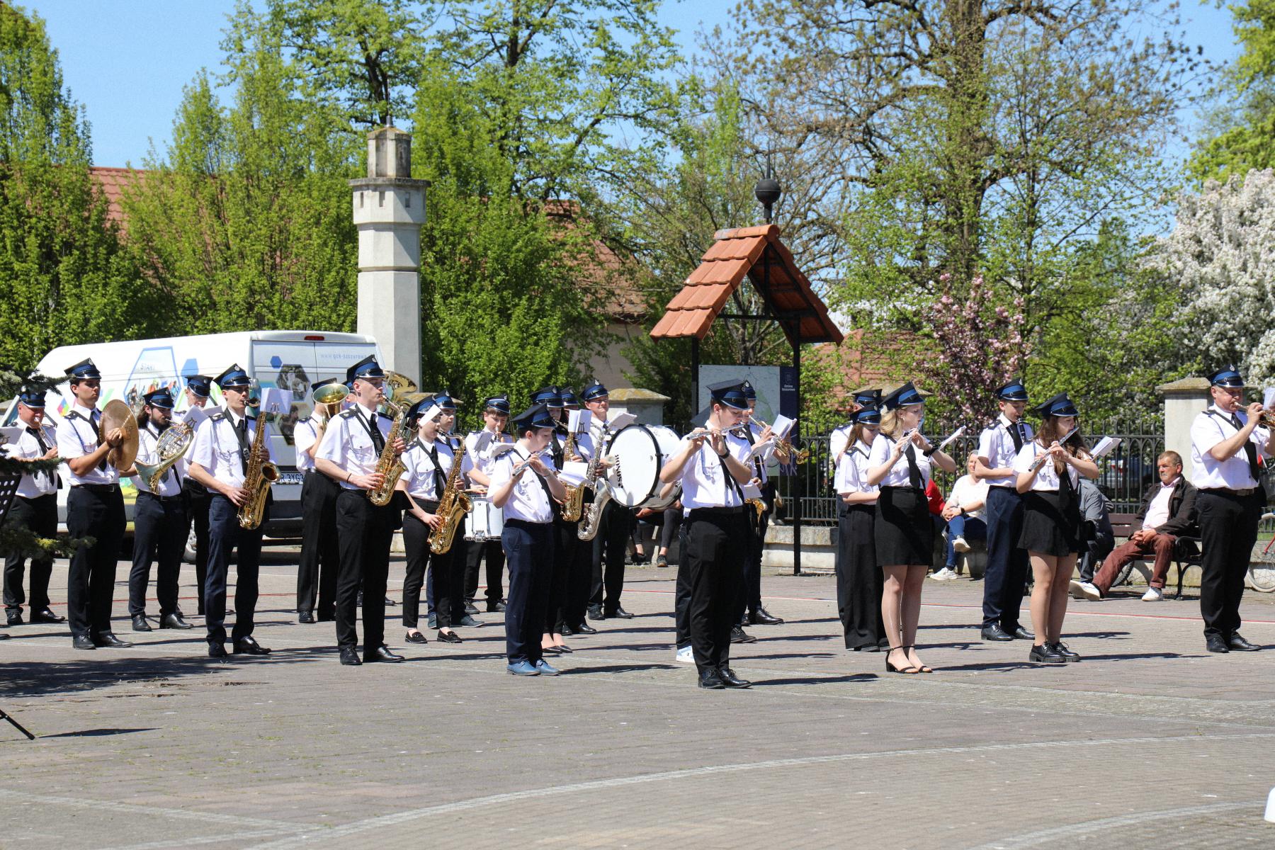 Na zdjeciu znajduje się orkiestra wykonująca koncert pod pomnikiem w Szczurowej